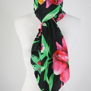May include: A black silk scarf with a floral print featuring pink, red, and yellow flowers on a green background.