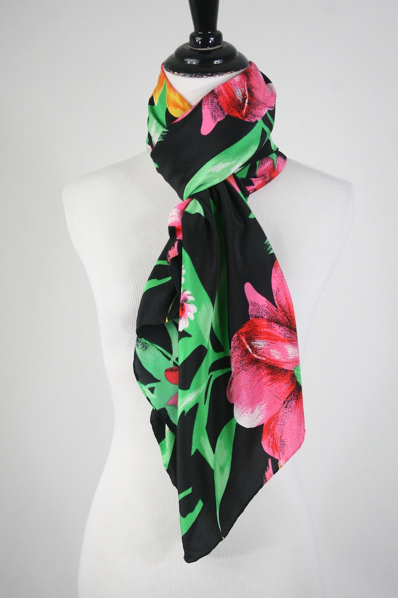May include: A black silk scarf with a floral print featuring pink, red, and yellow flowers on a green background.