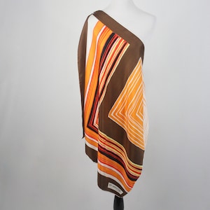 May include: A brown, orange, and white striped scarf with a geometric pattern. The scarf is draped over a white mannequin and has a "Guy Laroche" label.