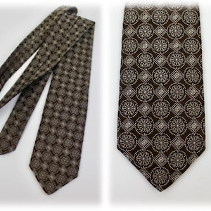May include: A brown tie with a repeating pattern of white and brown circular and square shapes. The tie is displayed in two views, one fully extended and the other folded. The background is white.