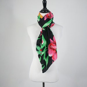 May include: A black silk scarf with a floral print of pink and green flowers. The scarf is tied around a white mannequin's neck.