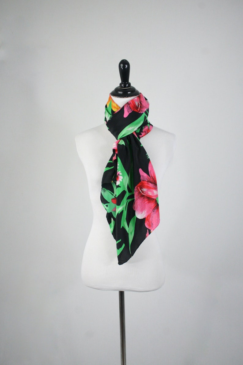 May include: A black silk scarf with a floral print of pink and green flowers. The scarf is tied around a white mannequin's neck.