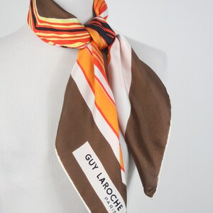 May include: A brown, white, and orange striped silk scarf with a white label that reads "GUY LAROCHE PARIS".