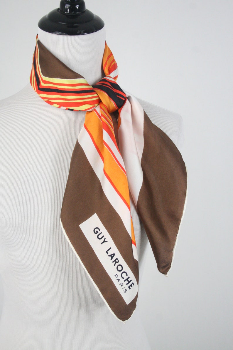 May include: A brown, white, and orange striped silk scarf with a white label that reads "GUY LAROCHE PARIS".