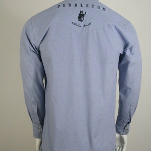 May include: A blue and white gingham long-sleeve shirt with a black embroidered logo on the back that says "PENDLETON" and features a rider on a horse. The logo also includes the text "Western Wear".