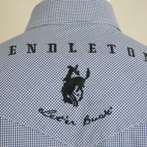 May include: A blue and white gingham shirt with a black embroidered Pendleton logo and the words "better buck" on the back.