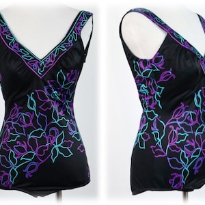 May include: Black swimsuit with a floral design in purple and turquoise. The swimsuit has a V-neck and thin straps.
