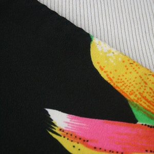 May include: Close-up of a black fabric with a colorful floral print. The print features yellow, orange, pink, and green flowers.
