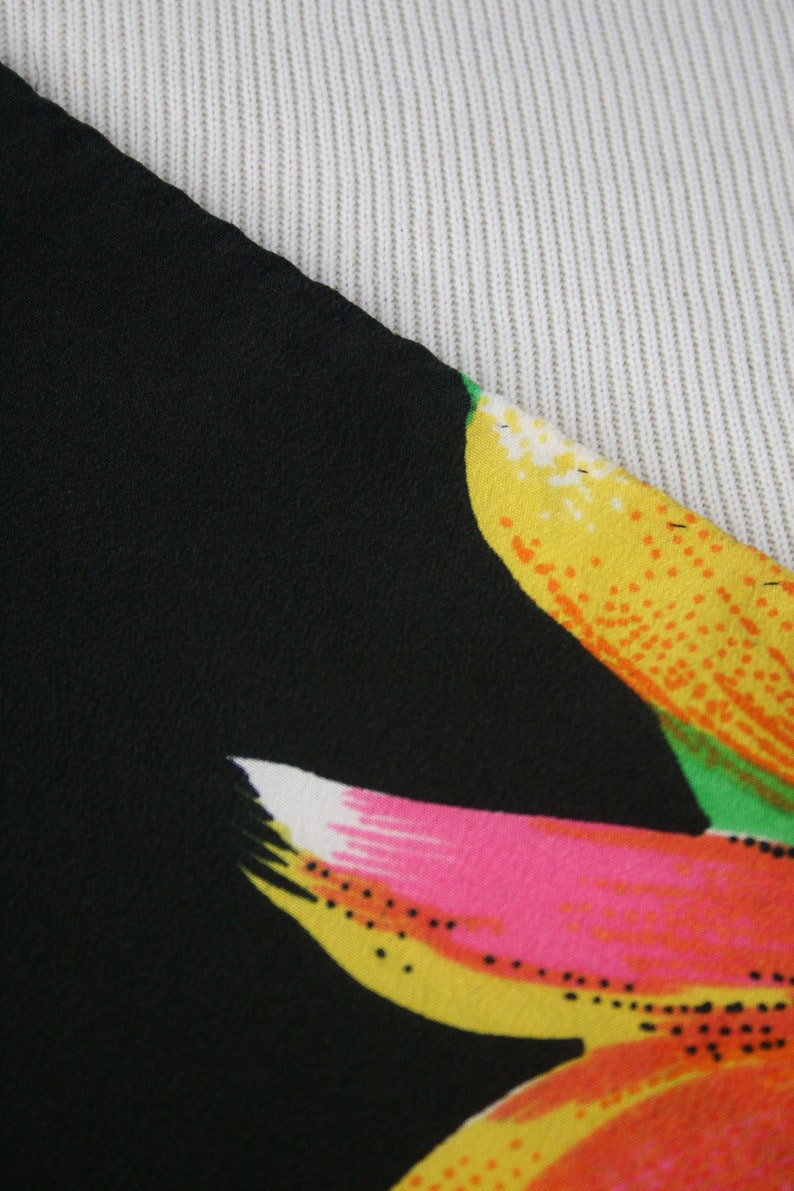 May include: Close-up of a black fabric with a colorful floral print. The print features yellow, orange, pink, and green flowers.