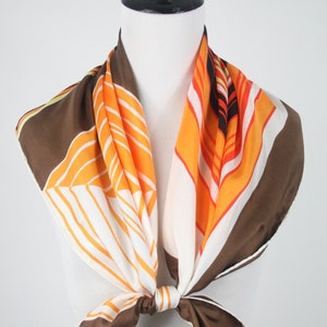 May include: A brown, orange, and white geometric patterned silk scarf tied around a mannequin's neck.