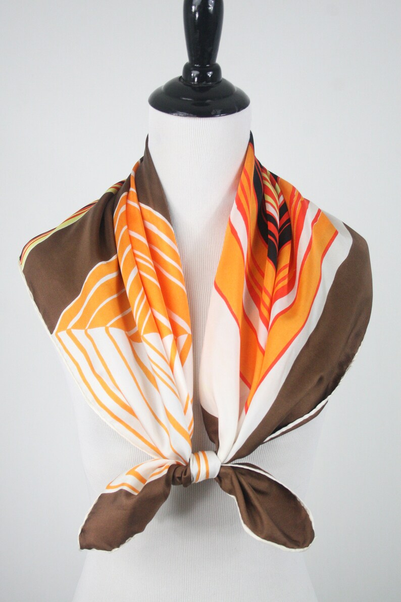 May include: A brown, orange, and white geometric patterned silk scarf tied around a mannequin's neck.