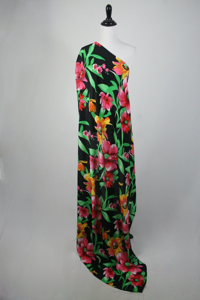 May include: Black fabric with a large floral print featuring pink, red, yellow, and green flowers. The fabric is draped over a mannequin.
