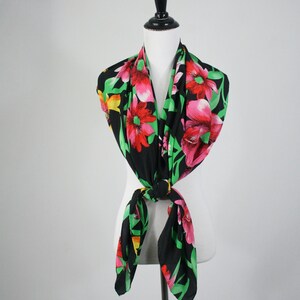 May include: A black silk scarf with a floral print featuring pink, red, and yellow flowers on a green background.