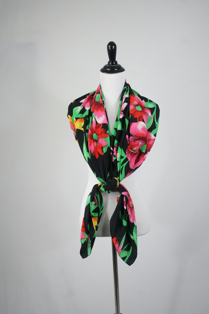 May include: A black silk scarf with a floral print featuring pink, red, and yellow flowers on a green background.