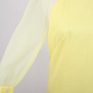 May include: A yellow dress with sheer, long sleeves. The dress has a high neckline and a fitted bodice.