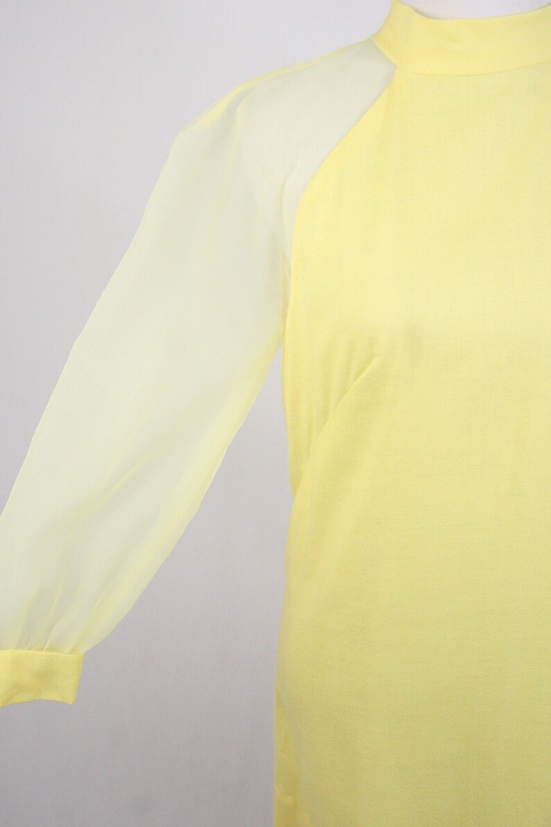 May include: A yellow dress with sheer, long sleeves. The dress has a high neckline and a fitted bodice.