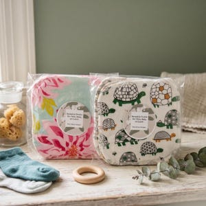 May include: Two packs of reusable baby cloths. One has a floral pattern in pink, yellow, and green. The other shows a turtle pattern in green and brown. The label reads "Reusable Cloths for Face, Baby, or Lunch".