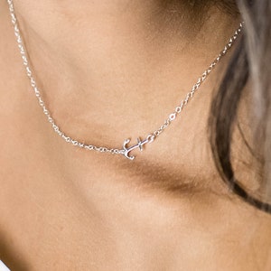 Puede incluir: Un collar de cadena de plata con un pequeño colgante de ancla.