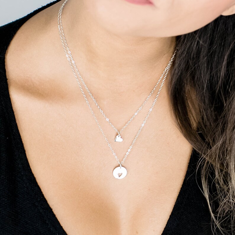 May include: A silver layered necklace with two heart pendants. The top pendant is a small heart, and the bottom pendant is a larger circle with a heart cut out.