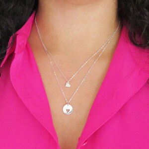 May include: A silver necklace with two pendants. The top pendant is a small heart, and the bottom pendant is a larger circle with a heart cut out of the center.
