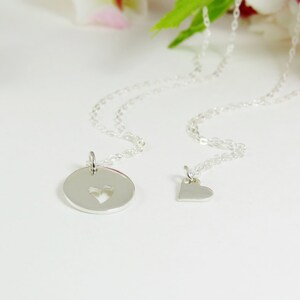May include: Two silver necklaces with heart-shaped pendants. One pendant is a circle with a heart cut out, the other is a solid heart.