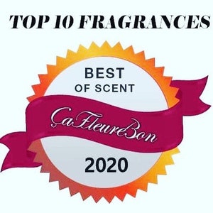 Może przedstawiać: Złota i pomarańczowa nagroda w kształcie rozgwiazdy z białym środkiem. W środku znajduje się tekst "Best of Scent" i "Ca Fleure Bon 2020". Wok&oacute;ł nagrody owija się czerwona wstążka z białym obramowaniem.