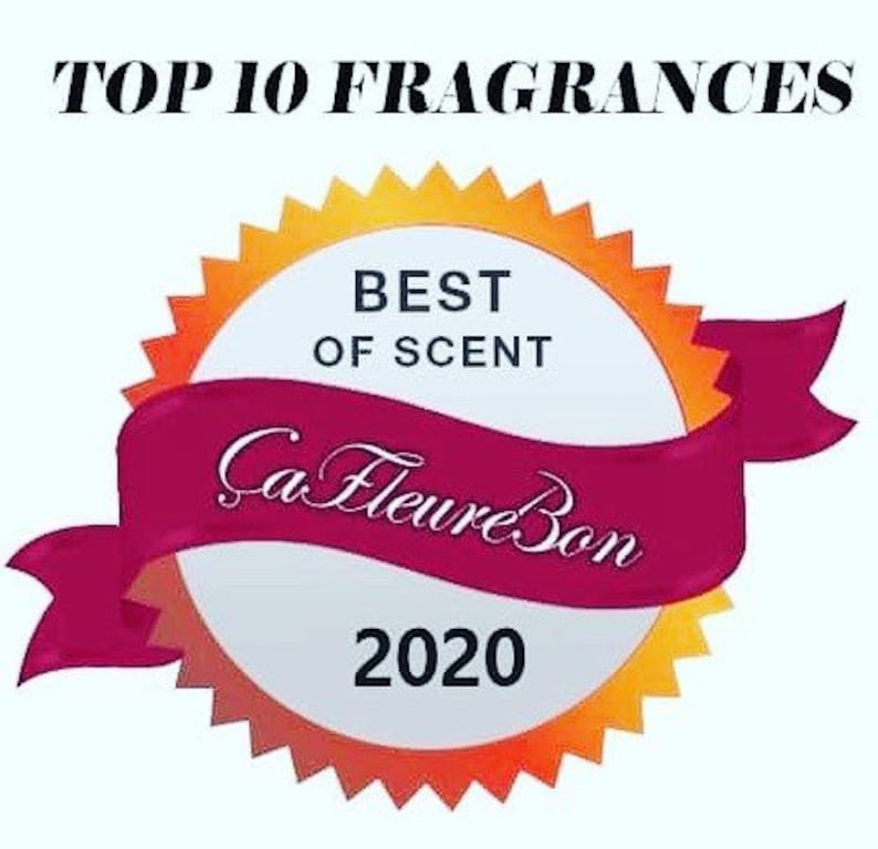 Może przedstawiać: Złota i pomarańczowa nagroda w kształcie rozgwiazdy z białym środkiem. W środku znajduje się tekst "Best of Scent" i "Ca Fleure Bon 2020". Wok&oacute;ł nagrody owija się czerwona wstążka z białym obramowaniem.