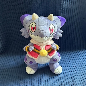 May include: Purple and white plush toy with horns, red eyes, and a yellow and brown patterned vest. The toy is standing on a blue surface.