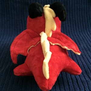 Overhead view of red dragon plushie showing wings, black horns, and yellow spikes