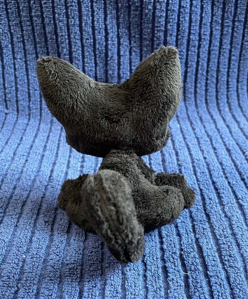 May include: A black plush cat toy sitting on a blue textured surface. The cat is sitting with its tail curled around its body.
