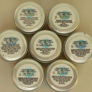 May include: Six small silver tins of Fairtrade Organic Cane Sugar Natural Lip Scrub in various flavours, including Double Chocolate, Prima Vera, and Lemon Sorbet. Each tin has a label with the product name and ingredients.