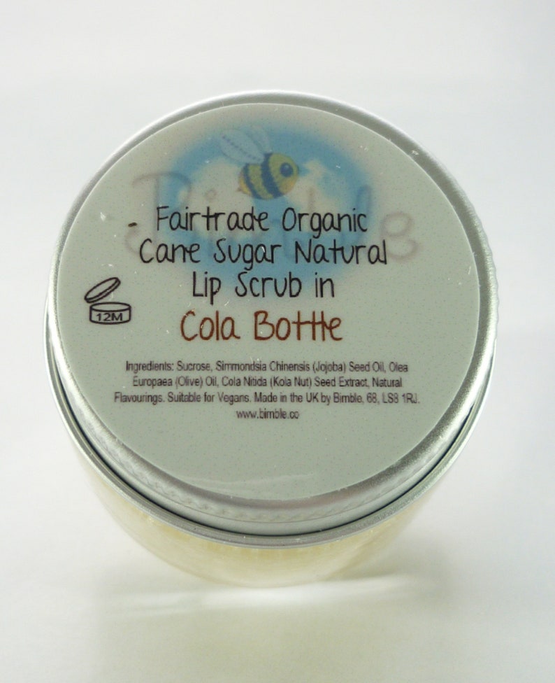 May include: A silver tin with a blue and white label that reads "Fairtrade Organic Cane Sugar Natural Lip Scrub in Cola Bottle". The label also includes a small bee illustration and the text "www.bimble.co".