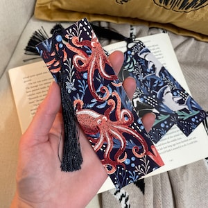 May include: A blue bookmark with a dark blue tassel features a colorful illustration of an octopus with a floral pattern. The octopus is red, orange, and white.