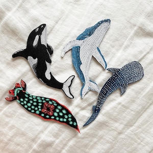 K&ouml;nnte beinhalten: Vier gestickte B&uuml;gelbilder mit Meeresmotiven: ein schwarz-wei&szlig;es Orca, ein blauer Wal, ein blauer und wei&szlig; gefleckter Walhai und eine rot-gr&uuml;ne Nacktschnecke.