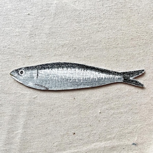 Peut inclure: Illustration d'un poisson argent&eacute; et noir. Le poisson pr&eacute;sente un motif de petits points noirs sur le dos et la queue, avec un corps argent&eacute; plus clair. Le fond est un tissu neutre et textur&eacute;.