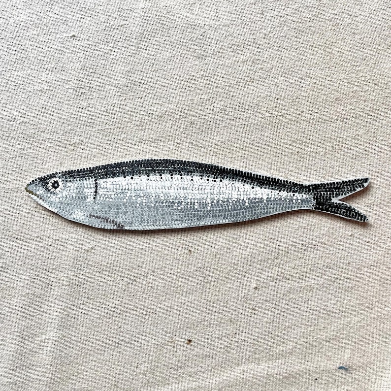Peut inclure: Illustration d'un poisson argent&eacute; et noir. Le poisson pr&eacute;sente un motif de petits points noirs sur le dos et la queue, avec un corps argent&eacute; plus clair. Le fond est un tissu neutre et textur&eacute;.