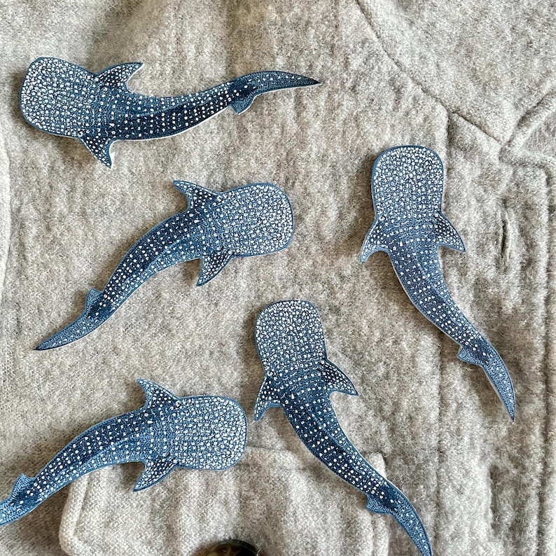 May include: Five blue whale shark cutouts with white dot patterns are arranged on a textured, light grey surface. The whale sharks have detailed fins and tails, and are in various positions.