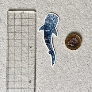 Puede incluir: Una pegatina de tibur&oacute;n ballena azul y blanca con un patr&oacute;n de manchas. La pegatina mide aproximadamente 5 cm de largo.
