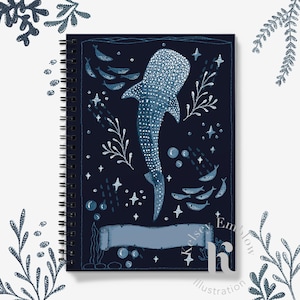 May include: A spiral-bound notebook with a whale shark illustration in blue and white on a dark blue backdrop. The design incorporates stars, bubbles, and marine life. The notebook has a dark spiral binding.