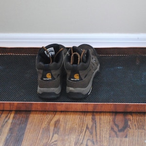 May include: A copper shoe tray with a black mesh insert. Two brown hiking boots are on the tray.