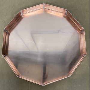 May include: Octagonal copper tray with a smooth, shiny surface. The tray has a slightly raised edge.
