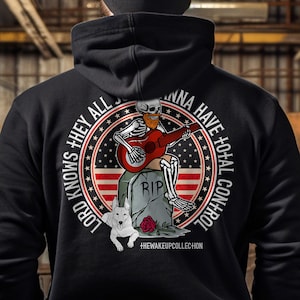 May include: Black hooded sweatshirt with a graphic print of a skeleton playing a guitar and a dog. The graphic is surrounded by a circle with the text "Lord knows they all wanna have total control" and a red, white, and blue American flag design.