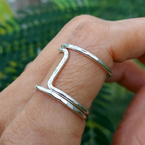 May include: A silver ring with a hammered finish and a unique, open design. The ring is worn on a finger.
