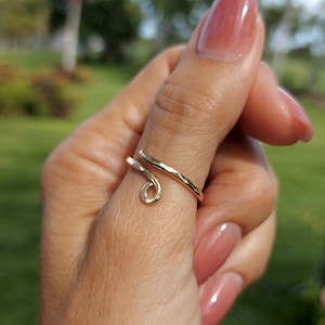 May include: A gold thumb ring with a hammered finish and a curved design. The ring is worn on a person's thumb.