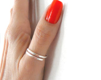 May include: A simple silver ring with a bypass design, featuring two parallel bands that overlap slightly. The ring is crafted from a smooth, polished metal with a reflective finish, creating a clean and understated look on the finger.