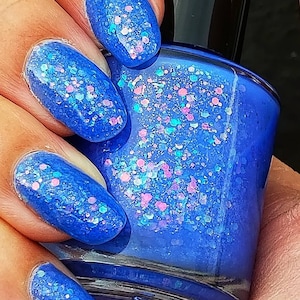 May include: A blue nail polish bottle with a sparkly, iridescent finish. The polish contains blue, pink, and white glitter.