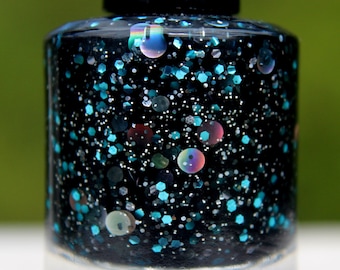 May include: A nail polish bottle with a black cap, filled with black polish and teal and iridescent glitter. The clear glass bottle contains a shimmering, textured liquid. The background is a blurred green. The polish creates a sparkling effect.