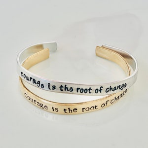 May include: Two silver and gold bracelets with the inscription "Courage is the root of change" on each.