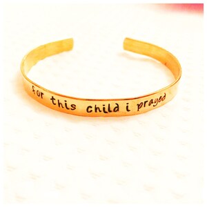 Puede incluir: Una pulsera de metal dorado con la inscripción "for this child I prayed".