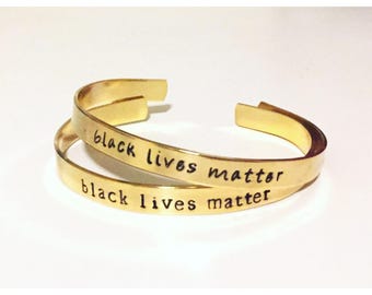 May include: Two gold bracelets with the words "black lives matter" engraved on them.